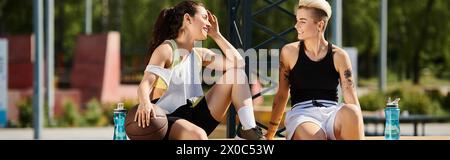 Zwei sportliche junge Frauen sitzen nebeneinander auf einer Bank im Freien. Stockfoto