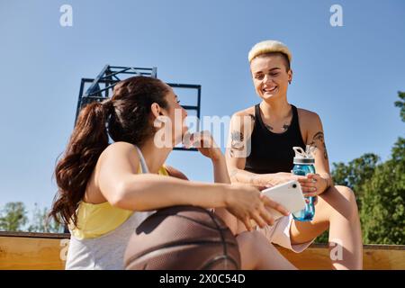 Zwei sportliche junge Frauen sitzen auf dem Boden und unterhalten sich, während sie eine Pause vom Basketball machen. Stockfoto