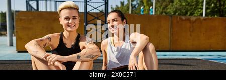 Zwei junge Frauen sitzen Seite an Seite und umarmen sich, nachdem sie an einem sonnigen Sommertag im Freien Basketball gespielt haben. Stockfoto