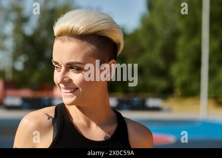 Eine junge Frau mit blonden Haaren und Tätowierungen, die ihre Sportlichkeit in einem schwarzen Tanktop zeigt. Stockfoto