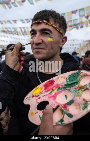 Diyarbakir, Türkei. März 2024. Ein junger Mann hat seine Wange mit einer Flagge bemalt, während ein anderer während einer Kundgebung beobachtet. Hunderttausende von Menschen besuchen Diyarbakir Newroz, um Newroz zu feiern, das die Ankunft des Frühlings und des neuen Jahres symbolisiert. Da es verboten ist, gelbe, grüne und rote Fahnen in Newroz zu bringen, malten die Menschen ihre Gesichter in gelben, roten und grünen Farben. (Foto: Bilal Seckin/SOPA Images/SIPA USA) Credit: SIPA USA/Alamy Live News Stockfoto