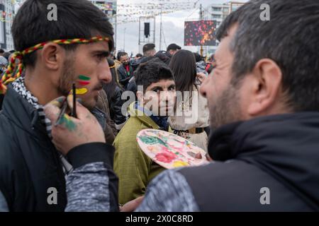 Diyarbakir, Türkei. März 2024. Ein junger Mann hat seine Wange mit einer Flagge bemalt, während ein anderer während einer Kundgebung beobachtet. Hunderttausende von Menschen besuchen Diyarbakir Newroz, um Newroz zu feiern, das die Ankunft des Frühlings und des neuen Jahres symbolisiert. Da es verboten ist, gelbe, grüne und rote Fahnen in Newroz zu bringen, malten die Menschen ihre Gesichter in gelben, roten und grünen Farben. (Foto: Bilal Seckin/SOPA Images/SIPA USA) Credit: SIPA USA/Alamy Live News Stockfoto