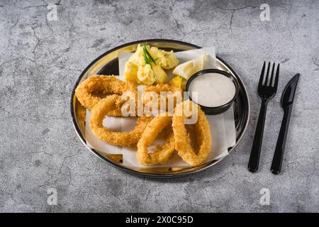 Gebratene Calamari mit Kartoffelsalat daneben auf Steintisch Stockfoto
