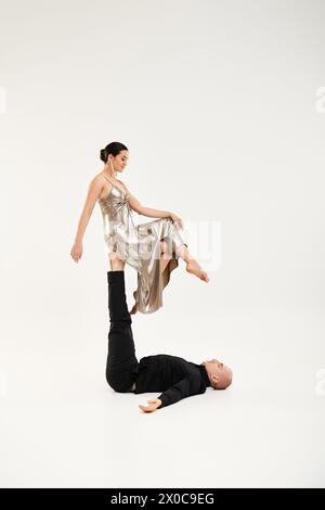 Ein junger Mann in Schwarz und eine junge Frau in einem glänzenden Kleid, die eine akrobatische Tanzroutine in einem Studio vor weißem Hintergrund aufführt. Stockfoto