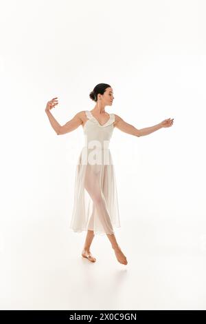 Eine junge Frau tanzt anmutig in einem langen weißen Kleid in einem Atelier-Setting vor weißem Hintergrund. Stockfoto