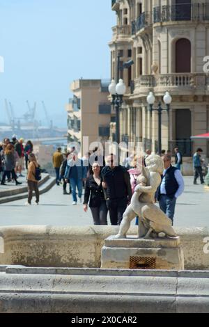 Tarragona, Spanien - 11. April 2024: Eine fesselnde Steinskulptur aus zwei ineinander verflochtenen Figuren, vor dem Hintergrund einer lebhaften Promenade und üppiger Vegetation Stockfoto