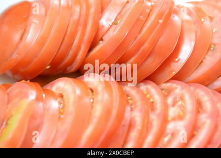 Ein Teller mit geschnittenen roten Tomaten. Die Schichten sind in einem ordentlichen Stapel angeordnet, wobei sich einige Schichten überlappen. Die Platte wird auf einen Tisch und die ima gelegt Stockfoto