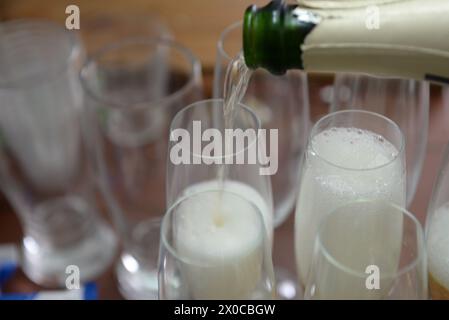 Eine Flasche Champagner wird in eine Reihe von Weingläsern gegossen. Das Konzept des Feierns und Genusses Stockfoto