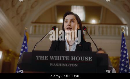 Seriöser Präsident der Vereinigten Staaten spricht auf einer Pressekonferenz im Weißen Haus für Medien- und Fernsehnachrichten. Eine Politikerin spricht inspirierende Rede aus. Amerikanische Fahnen im Hintergrund. Stockfoto