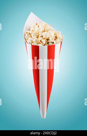 Popcorn in rot-weiß gestreiftem Papierkegel auf blauem Hintergrund. Stockfoto