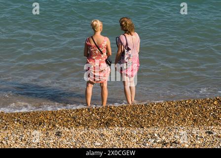 Freundinnen Eastbourne Beach 2 Frauen unterhalten sich, sie haben ihre Schuhe ausgezogen und stehen am Ufer. Sie haben ihre Sommerkleider hochgezogen, damit sie nicht nass werden. Eastbourne, East Sussex, England, 28. August 2013. HOMER SYKES AUS DEN 2010ER JAHREN Stockfoto