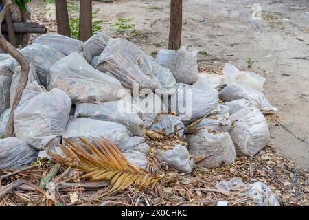 Gestapelte Blätter, die in großen weißen Plastiktüten im Hinterhof gesammelt wurden. Laubentfernung in der Stadtstraße oder im Park. Entsorgung von Naturabfällen. Stockfoto