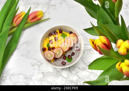 Chiasamen Dessert mit Früchten, umgeben von gelben und roten Tulpen. Draufsicht. Stockfoto