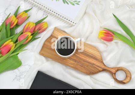 Schwarzer Kaffee auf einem Holztablett mit gelben und roten Tulpen. Romantisch. Stockfoto