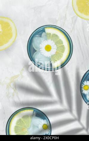 Getränke in blauen Gläsern, dekoriert mit Blumen und Zitronenscheiben. Draufsicht, über Blattschatten. Stockfoto