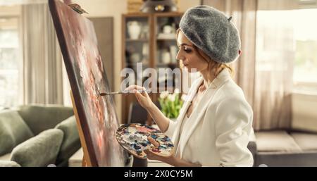 Schöne Malerin genießt beim Malen im Kunststudio zu Hause. Die Künstlerin arbeitet an abstrakter Acrylmalerei im Atelier. Stockfoto