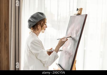 Schöne Malerin genießt beim Malen im Kunststudio zu Hause. Die Künstlerin arbeitet an abstrakter Acrylmalerei im Atelier. Stockfoto