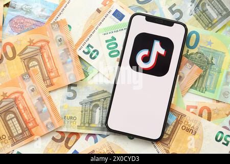 KIEW, UKRAINE - 1. APRIL 2024 TikTok- oder Douyin-Symbol auf dem Smartphone-Bildschirm auf vielen Euro-Geldscheinen. IPhone-Display mit App-Logo mit Euro-Banknoten in europäischer Währung Stockfoto