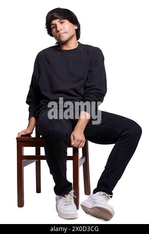 Latino-Mann in Schwarz posiert für ein Fotoshooting. Er sitzt auf einem Holzstuhl, der Hintergrund ist weiß. Stockfoto