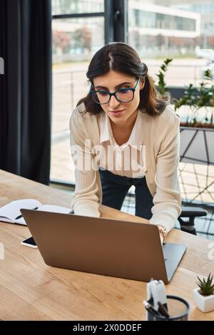 Eine Geschäftsfrau mit Brille konzentriert sich auf ihren Laptop und verwaltet ein Franchise in einem modernen Büroarbeitsplatz. Stockfoto