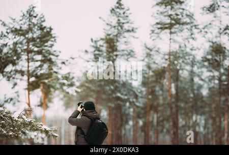 Junger Mann Backpacker mit Foto Kamera nimmt Fotos im Winter schneebedeckten Wald. Aktive Hobby. Wanderer Wandern in Verschneiten Pinienwald Stockfoto