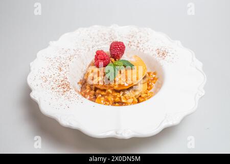Flauschige Pfannkuchen mit Himbeeren und Minzblättern auf einer weißen Platte vor einem sauberen weißen Hintergrund. Nahaufnahme. Stockfoto