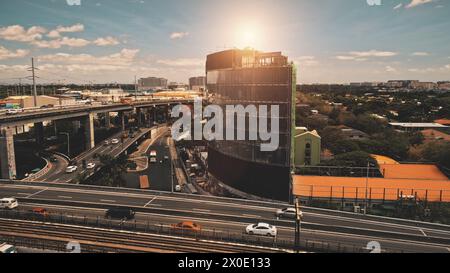 Nahaufnahme Sonne Stadt: Verkehrsstraße mit Autos an Wolkenkratzern Luft. Moderne Gebäude am Straßenrand. Manila Stadtstraßen des Business Centers bei Sonnenlicht. Philippinen-Metropole bei Nahaufnahme Stockfoto