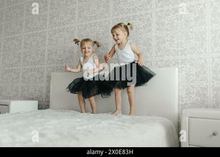 Zwei junge Mädchen in lässiger Kleidung springen glücklich auf ein Bett in einem Schlafzimmer. Stockfoto