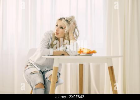 Eine Frau sitzt an einem Tisch mit einem Teller Persimmonen vor sich. Stockfoto