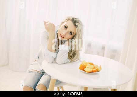 Eine Frau sitzt an einem Tisch mit einem Teller Persimmonen vor sich. Stockfoto