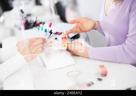 Manikuristin hilft Frau Client, die Farbe des Nagellacks auf Palette zu wählen Stockfoto