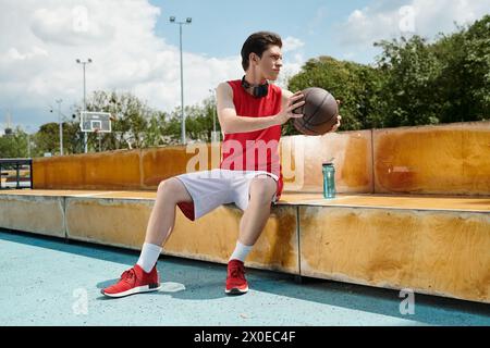 Ein junger Mann, der auf einer Bank sitzt, tief in Gedanken, an einem sonnigen Tag einen Basketball hält. Stockfoto