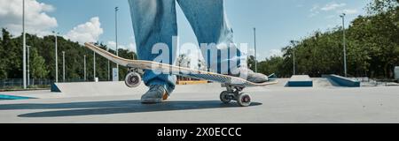 Ein junger Skater fährt mühelos auf seinem Skateboard und führt an einem sonnigen Sommertag Tricks im pulsierenden Skatepark durch. Stockfoto