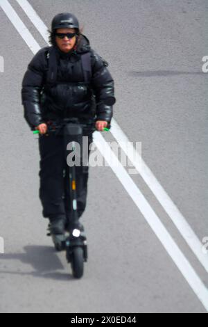 Tarragona, Spanien - 11. April 2024: Person in schwarzem Outfit und Helm fährt auf einer markierten Straße mit einem Elektroroller und zeigt eine moderne und ökologische Stadt Stockfoto