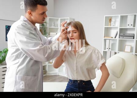 Männlicher Arzt, der ein medizinisches Pflaster auf den Kopf der Frau mit Gehirnerschütterung in der Klinik aufbringt Stockfoto