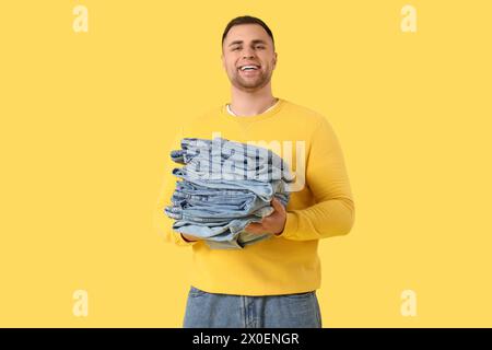 Junger Mann mit einem Stapel Jeans auf gelbem Hintergrund Stockfoto