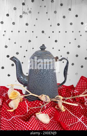 Teekaffeekanne sitzt auf rotem Polkadot-Tuch mit Milchkraut als Tischdekoration. Hintergrund zeigt Sterndesign mit Löchern in weißem Sitzbrett. Entspannter Urlaub. Stockfoto
