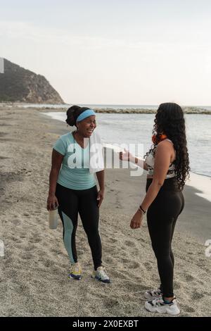 Zwei Frauen lachen während einer Fitnesspause an einem abgeschiedenen Strand. Stockfoto