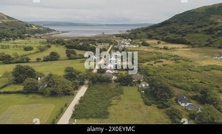 Zeitlupe der schottischen Whisky-Destillerie in Village Aerial. Straße, Hütten, Häuser im grünen Bergtal. Sommer bewölkter Tag. Keine Naturlandschaft auf Arran Island, Schottland. Filmdrohnenaufnahme Stockfoto