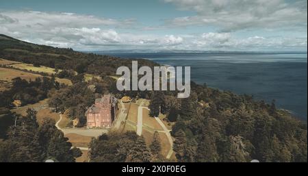 Schottlands Landschaft, mittelalterliche Burg aus der Vogelperspektive: Bäume und Meeresufer in Brodick Bay, Arran Island. Majestätische Landschaft mit grünem Laubwald an der Küste. Schönheit der schottischen Natur. Kinoaufnahme Stockfoto