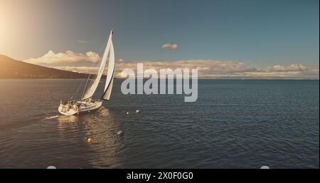 Sonne über Segelregatta auf Luxusyachten aus der Luft. Filmisches Seeblick am sonnigen Sommertag. Majestätische Segelboote fahren an der Meeresbucht im Hafen von Brodick, Arran Island, Schottland. Panorama-Drohne aufgenommen Stockfoto