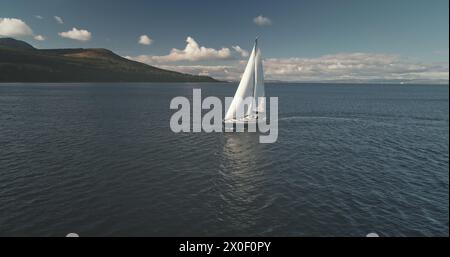 Sonnenspiegelung auf dem Segelboot in der Meereslandschaft. Rennyacht segelt auf offener See. Luxusschiff bei einer Sommer-Bootstour auf Arran Island, Schottland, Europa. Filmisches sanftes Sonnenlicht über dem ruhigen Wasser der Meeresbucht Stockfoto