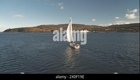 Zeitlupe der Yachtspiegelung an der Meeresgulftrolle. Allein Segelboot reflektiert in der Meeresbucht. Rennsegelboot am Brodick Harbor, Schottland, Europa. Luxusschiff auf Sommerkreuzfahrt. Filmische Aufnahmen mit weichem Licht Stockfoto