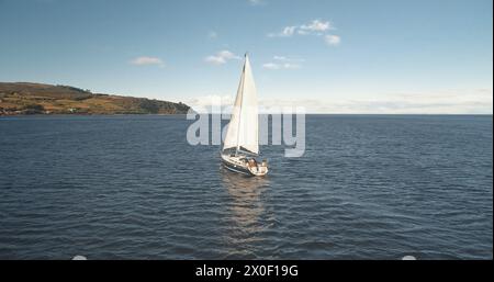 Zeitlupe der Yachtspiegelung an der Meeresgulftrolle. Allein Segelboot reflektiert in der Meeresbucht. Rennsegelboot am Brodick Harbor, Schottland, Europa. Luxusschiff auf Sommerkreuzfahrt. Filmische Aufnahmen mit weichem Licht Stockfoto