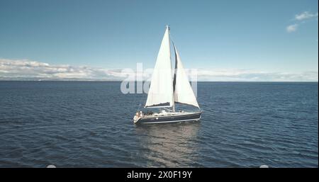 Zeitlupe der Yachtspiegelung an der Meeresgulftrolle. Allein Segelboot reflektiert in der Meeresbucht. Rennsegelboot am Brodick Harbor, Schottland, Europa. Luxusschiff auf Sommerkreuzfahrt. Filmische Aufnahmen mit weichem Licht Stockfoto