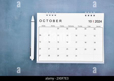 Direkt über Ansicht des Schreibtischkalenders Oktober 2024 und Stift auf blauem Holzhintergrund. Stockfoto