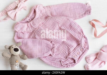 Rosafarbener Strickbody mit Spielzeug gestricktem Hund, Socken und Stirnband. Set von Babykleidung und Accessoires Sommer auf weißem Holz Hintergrund. Fashion Neugeborene Stockfoto