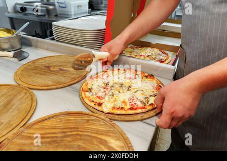 Der Koch schneidet frisch gebackene Pizza in einer kommerziellen Küche Stockfoto