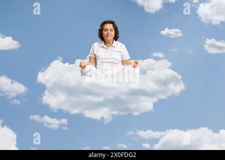 Ältere Frau, die auf einer Wolke am blauen Himmel meditiert Stockfoto