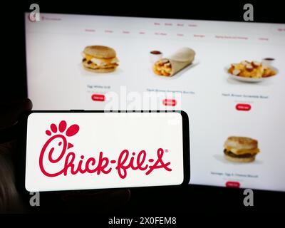 Person mit Smartphone und Logo des US-amerikanischen Fast-Food-Restaurantunternehmens Chick-Fil-A Inc. Vor der Website. Schwerpunkt auf dem Display des Telefons. Stockfoto